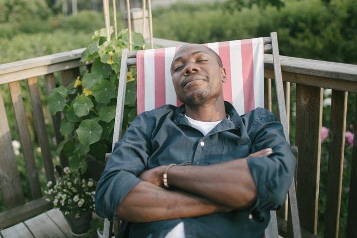Mid adult man with closed eyes taking a nap on deck chair at porch