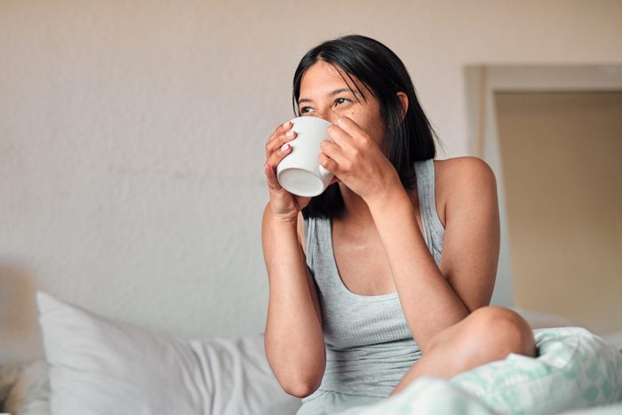 young woman drinking tea on a hotel room bed