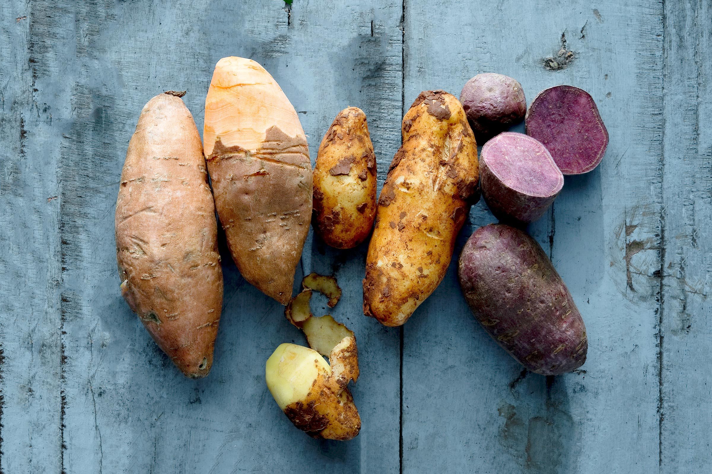 different varieties of potatoes lying on wooden surface