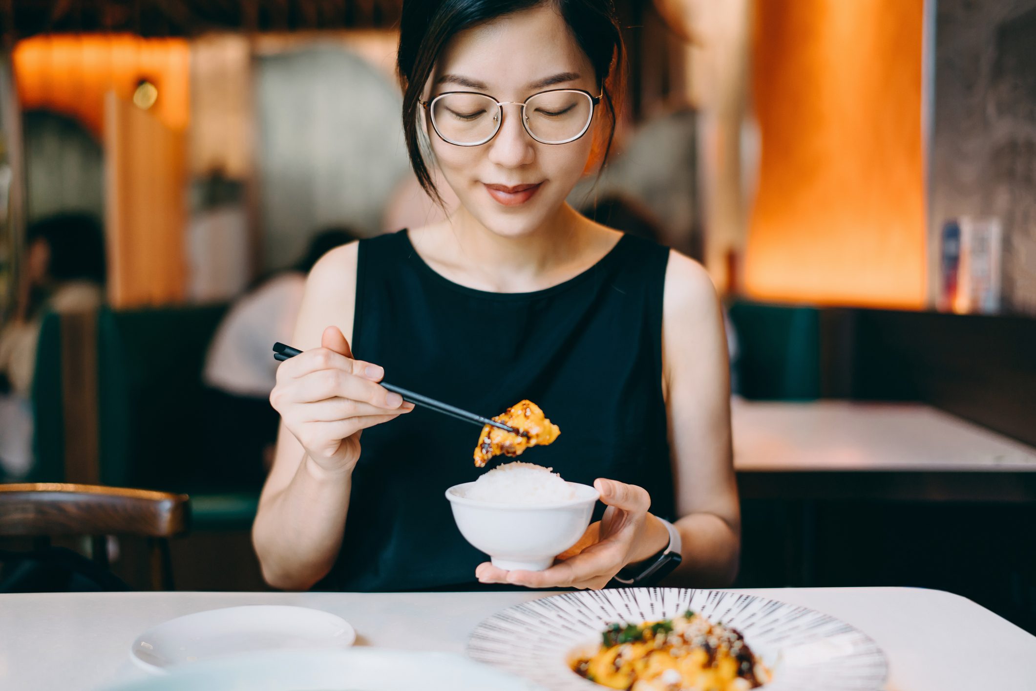 Smiling young Asian woman enjoying traditional Chinese Szechuan cuisine, spicy chicken in chilli oil in a restaurant. Asian food and cuisine