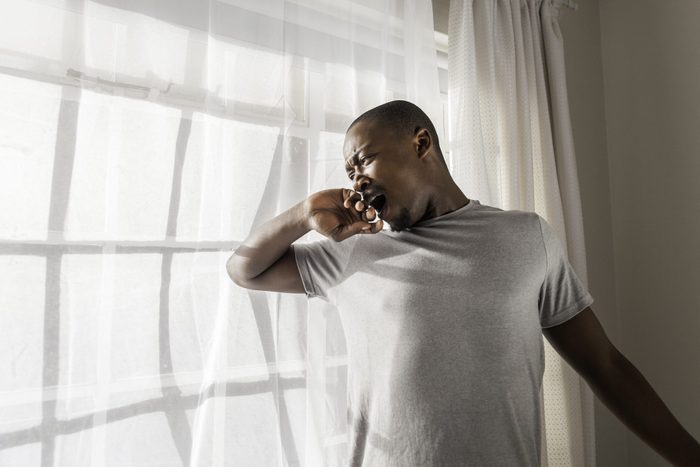 Mid adult African businessman fresh out of bad getting up for work in the morning, he stretching and yawning.