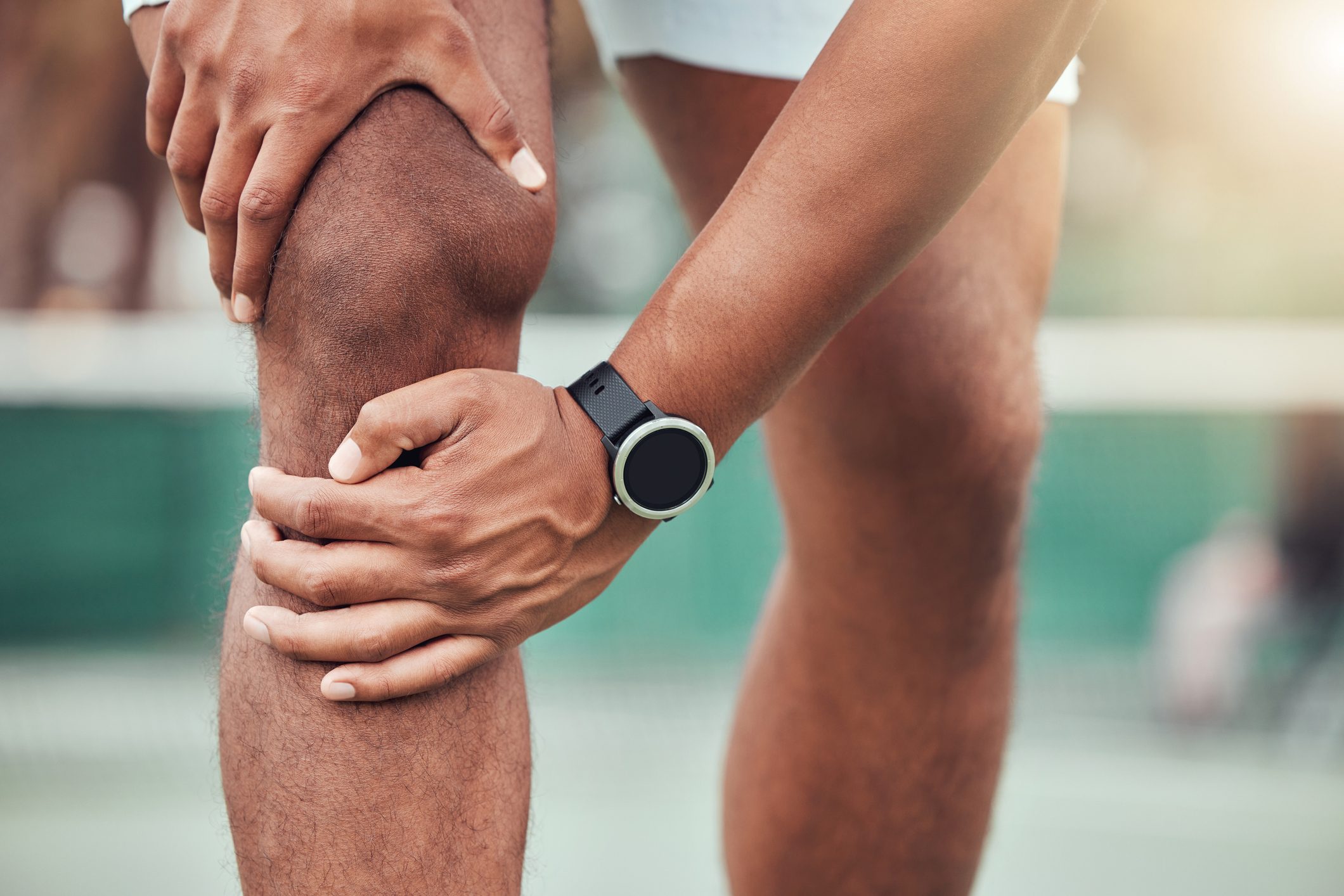 Closeup of unknown indian tennis player suffering from knee injury in court game. Ethnic fit professional in pain while holding and rubbing leg after match. Sporty man standing alone in sports club