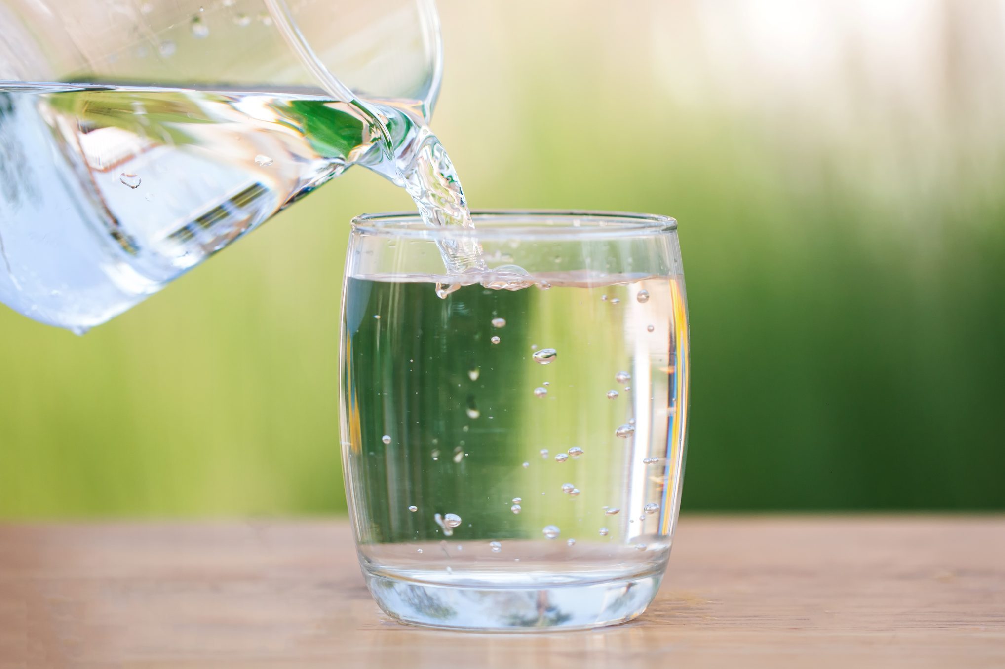 pouring water from a clear glass pitcher into a clear glass cup