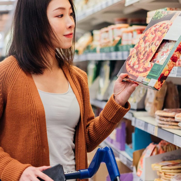 Young Asian woman picking up a packaged pizza in grocery store