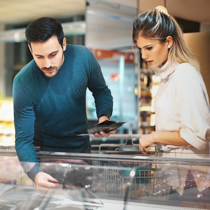 couple at the supermarket tanding un front of large open top freezer and picking up some unrecognizable products