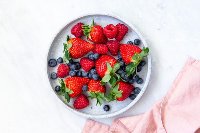 Mixed berries in conrete plate on marble background with empty plate and copy space