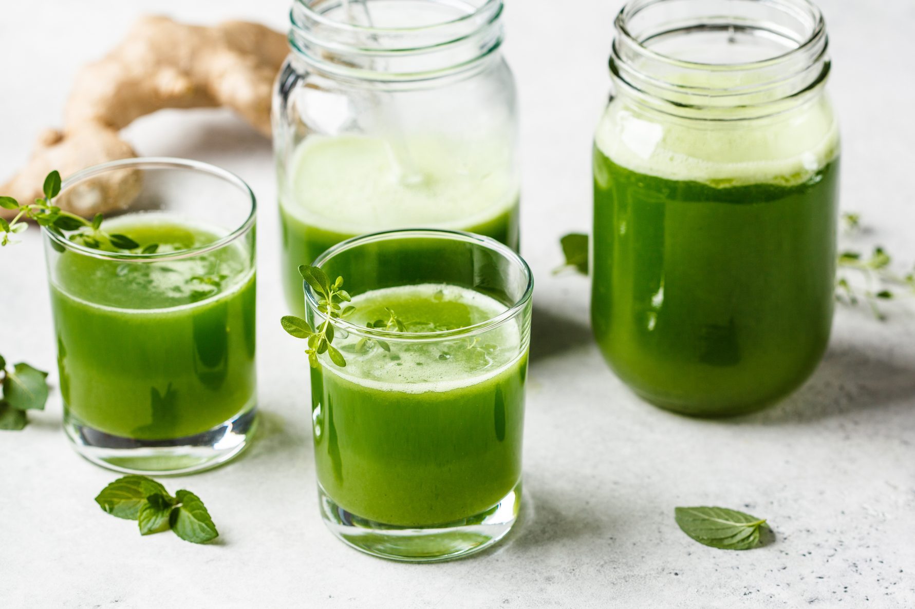 Green detox juice with ginger and mint in glasses and jars.