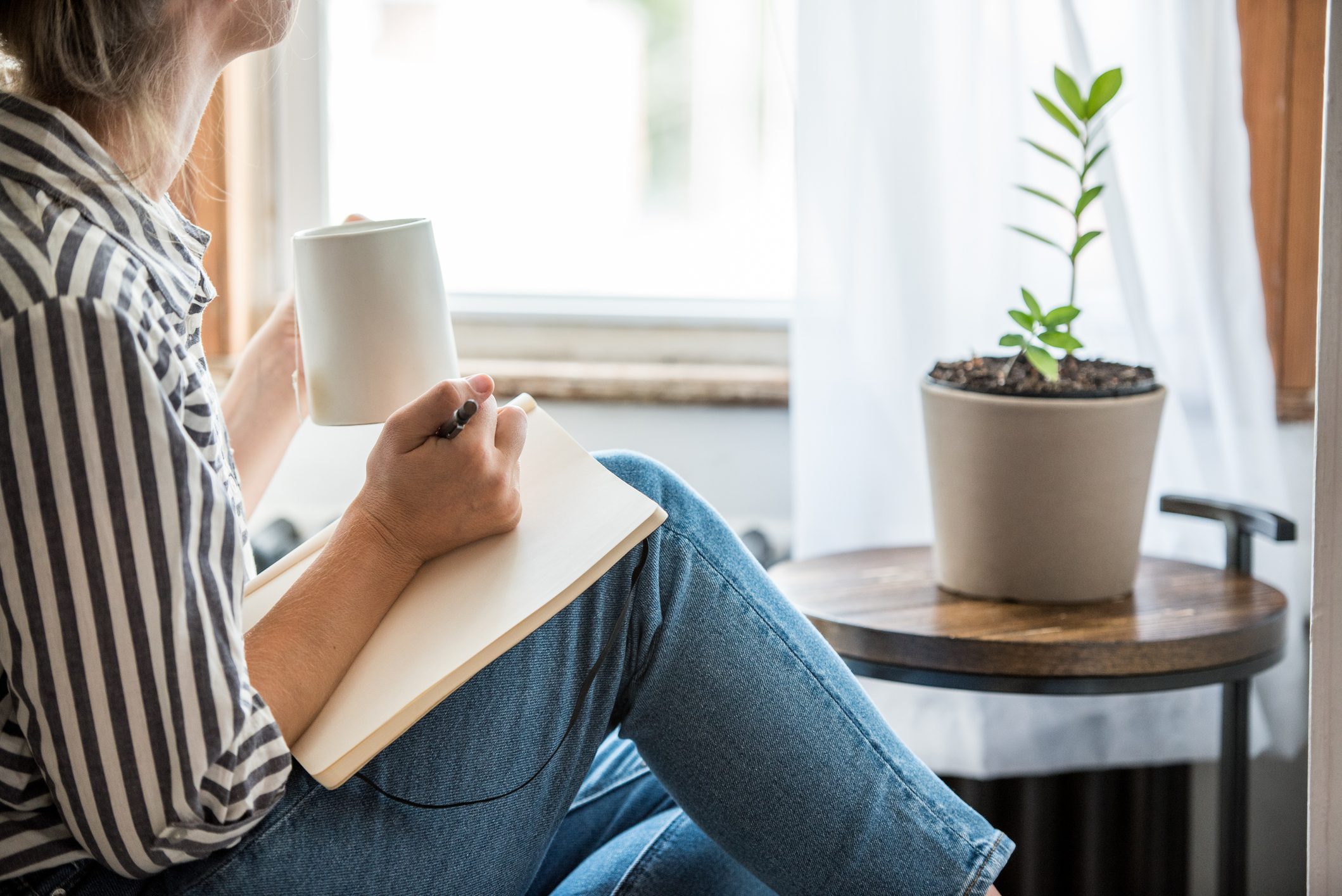 A young woman writing in her journal and drinking tea