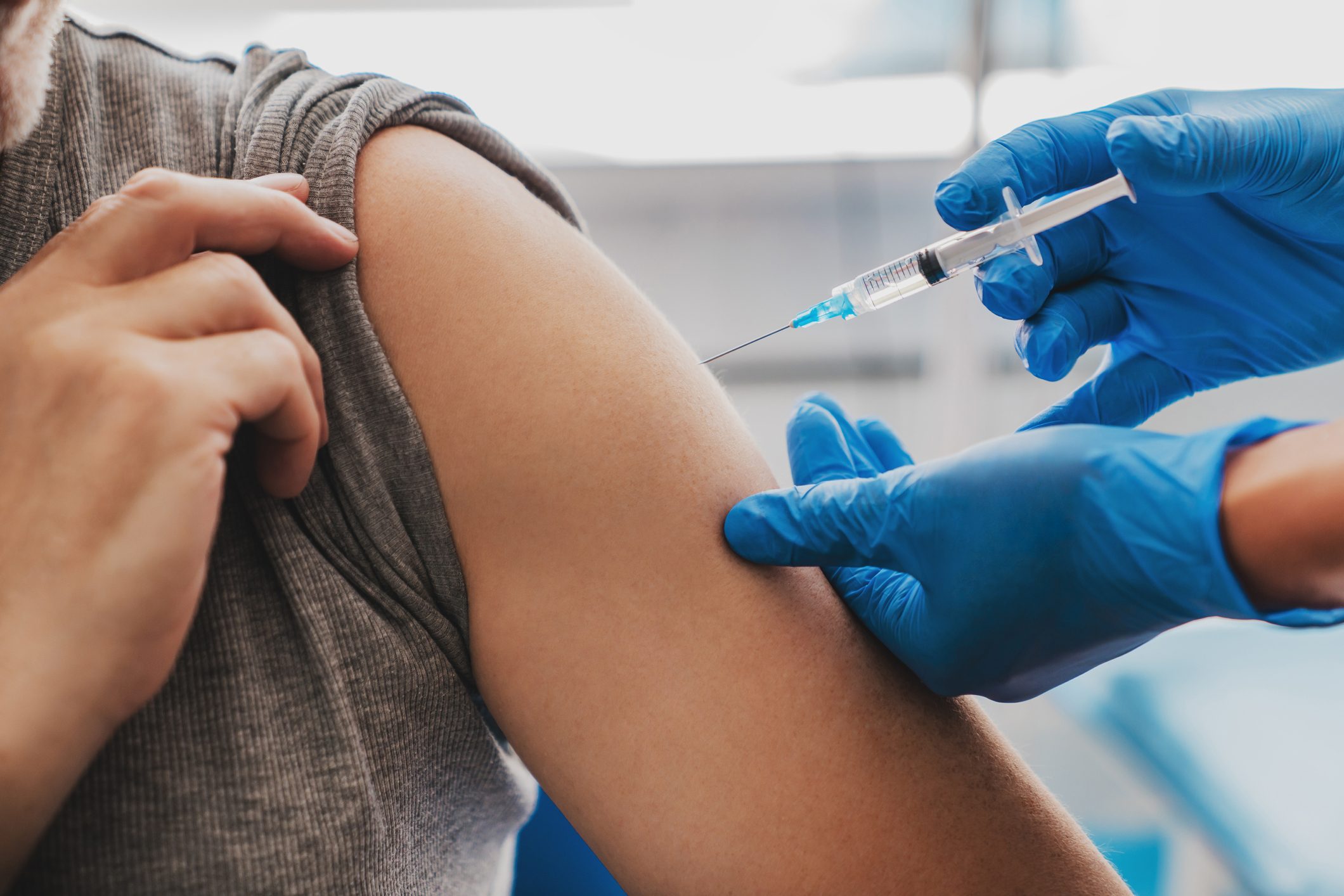 close up of a gloved hand giving a shot in someones arm as they roll up their sleeve