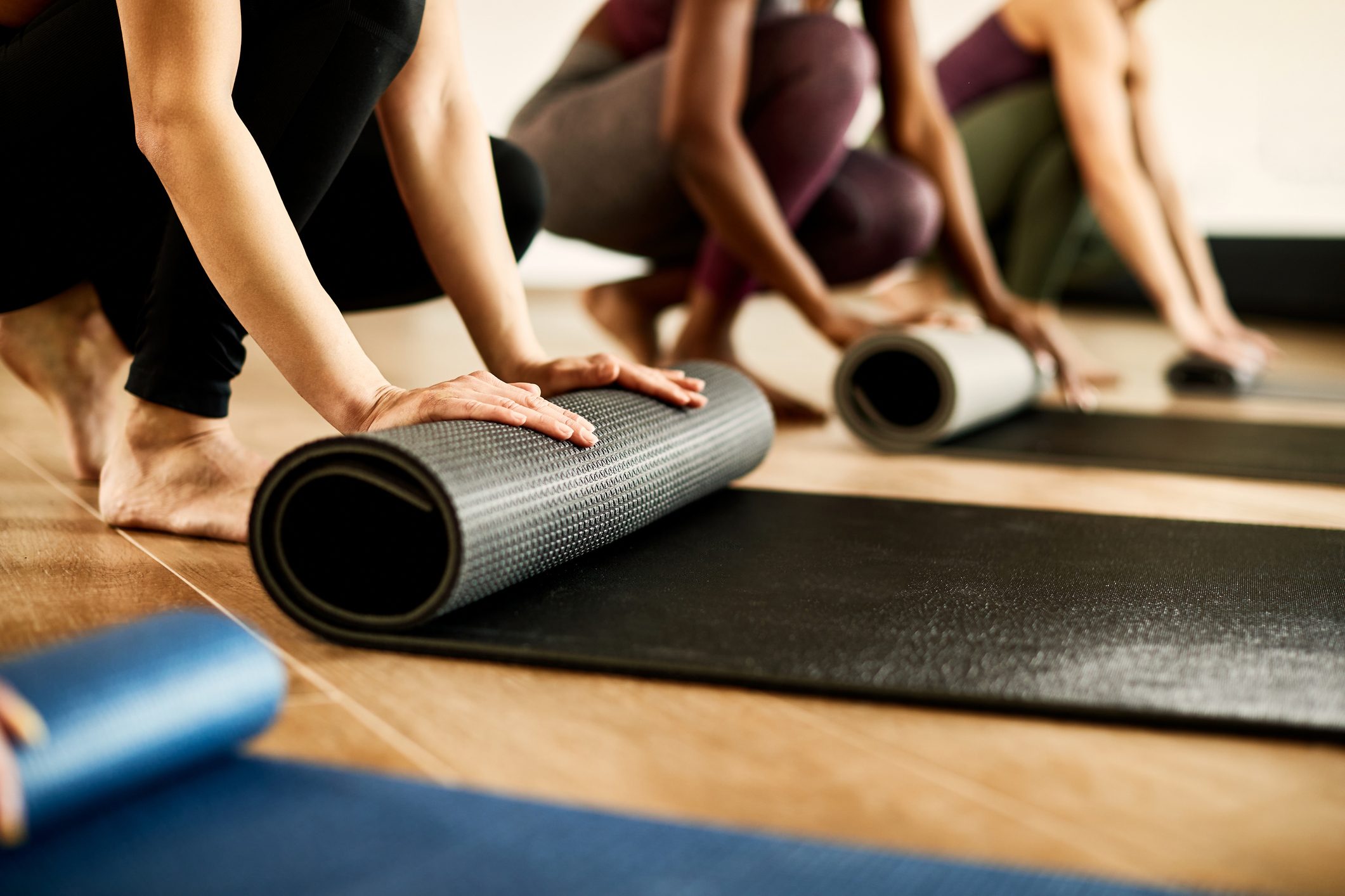 Close-up of athletic woman rolling up her exercise mat after practicing at health club.