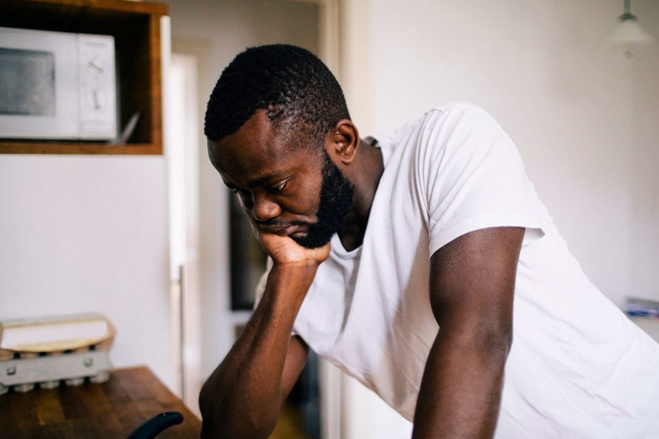 Thoughtful lonely man with hand on chin leaning in kitchen at home