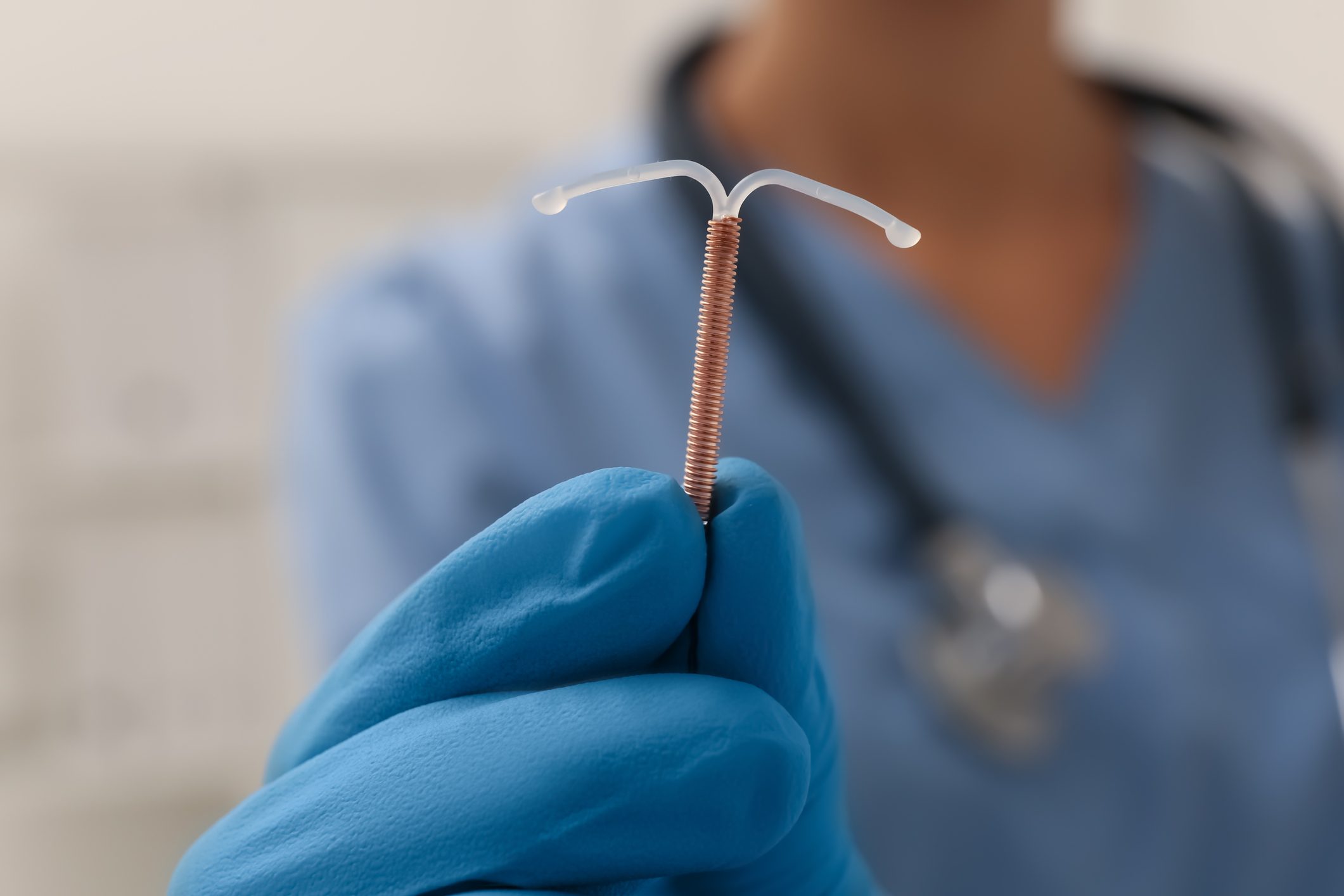 anonymous Doctor holding T-shaped intrauterine birth control device on blurred background, closeup