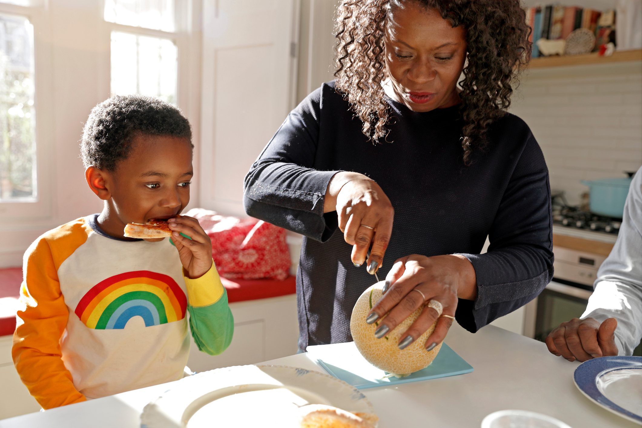 Mother cutting cantaloup and son sitting at the counter in the kitchen