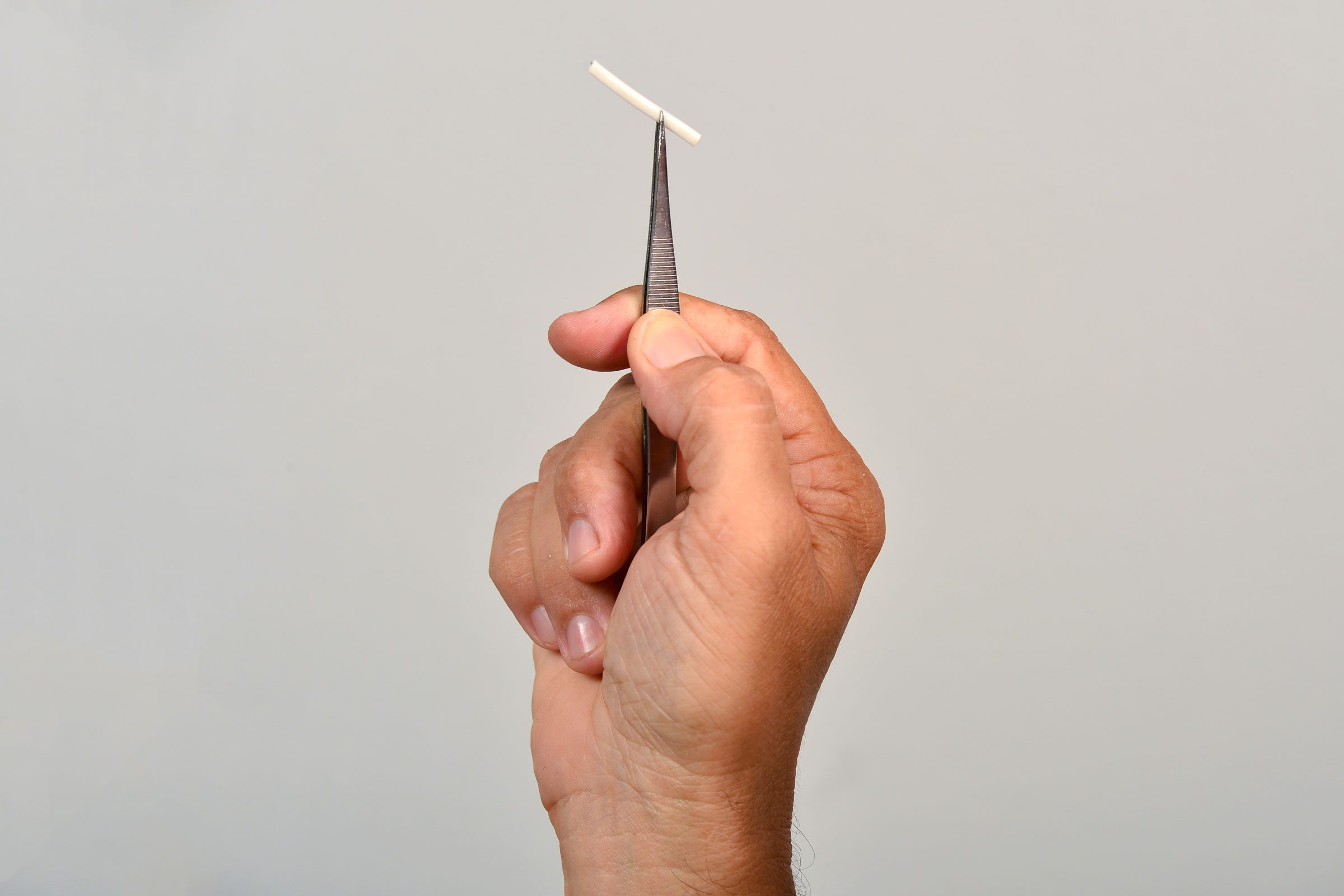 a hand holding a birth control arm implant in a pair of tweezers