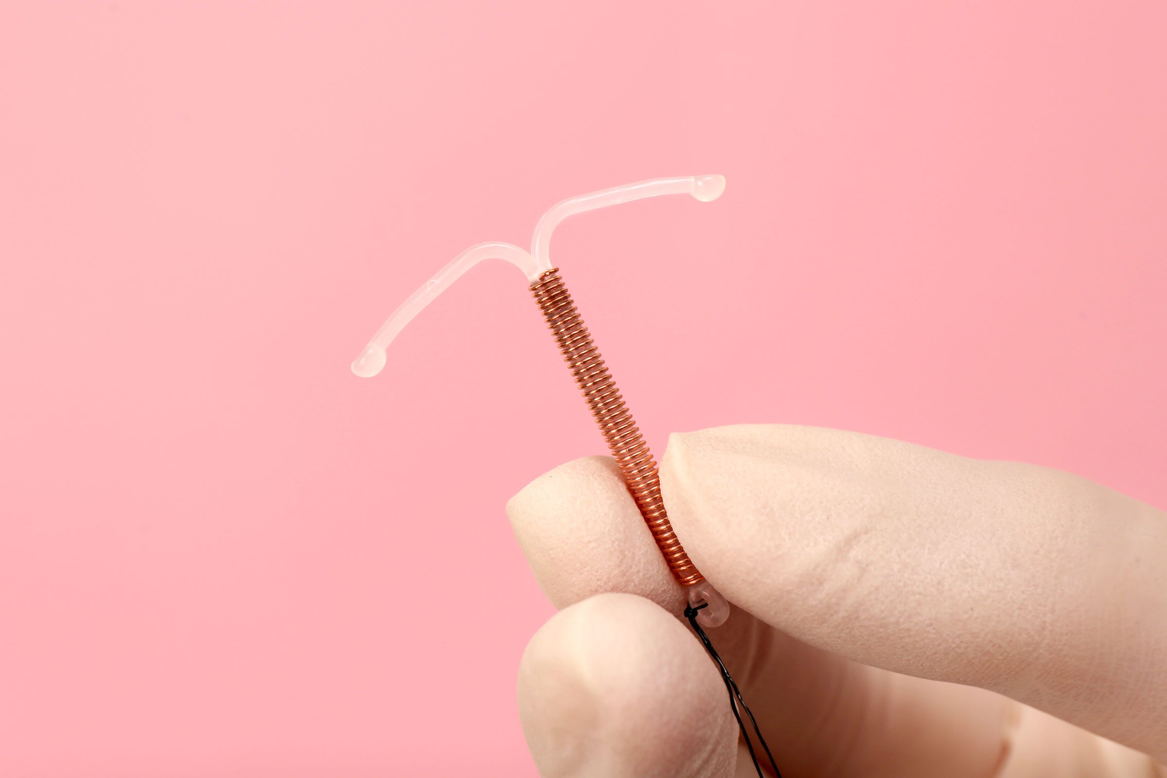 gloved hand holding a Hormonal Iud against a pink background