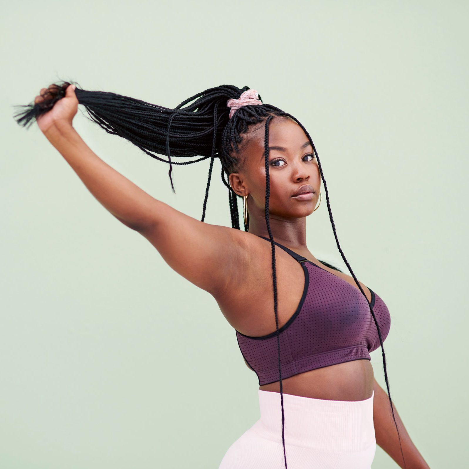 Cropped studio portrait of a young woman pulling her hair and posing against a green background