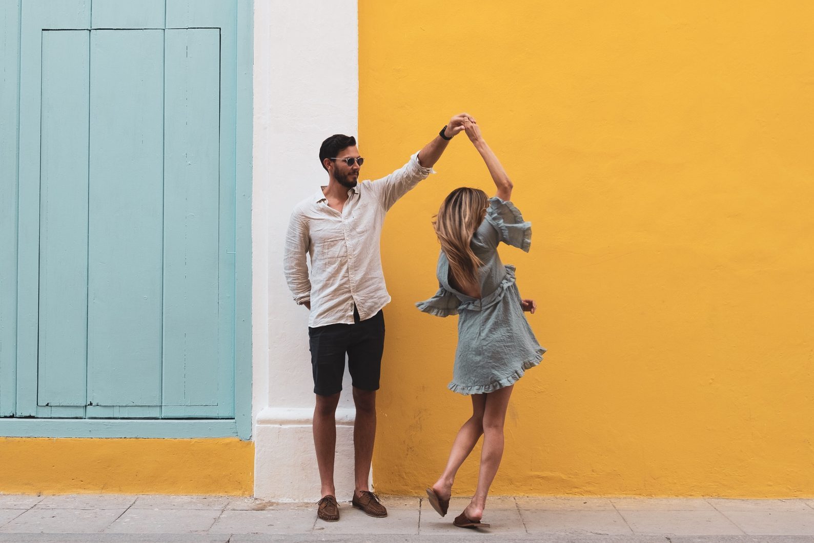 Full Length Of Couple Dancing On Sidewalk Against Yellow Wall