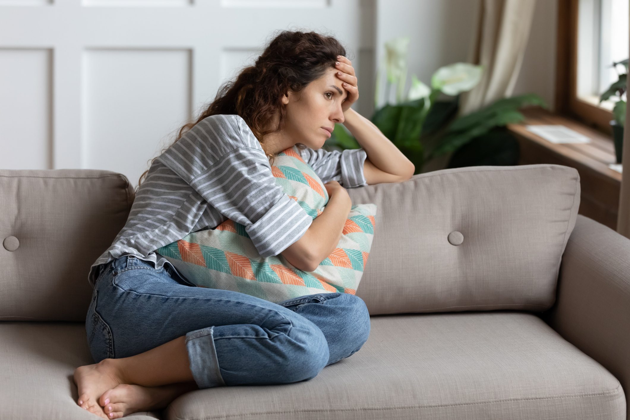 unhappy and stressed woman sitting on a couch at home with a pillow