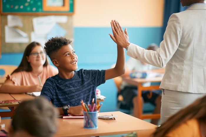Happy black elementary student and his teacher giving high five during class at school.
