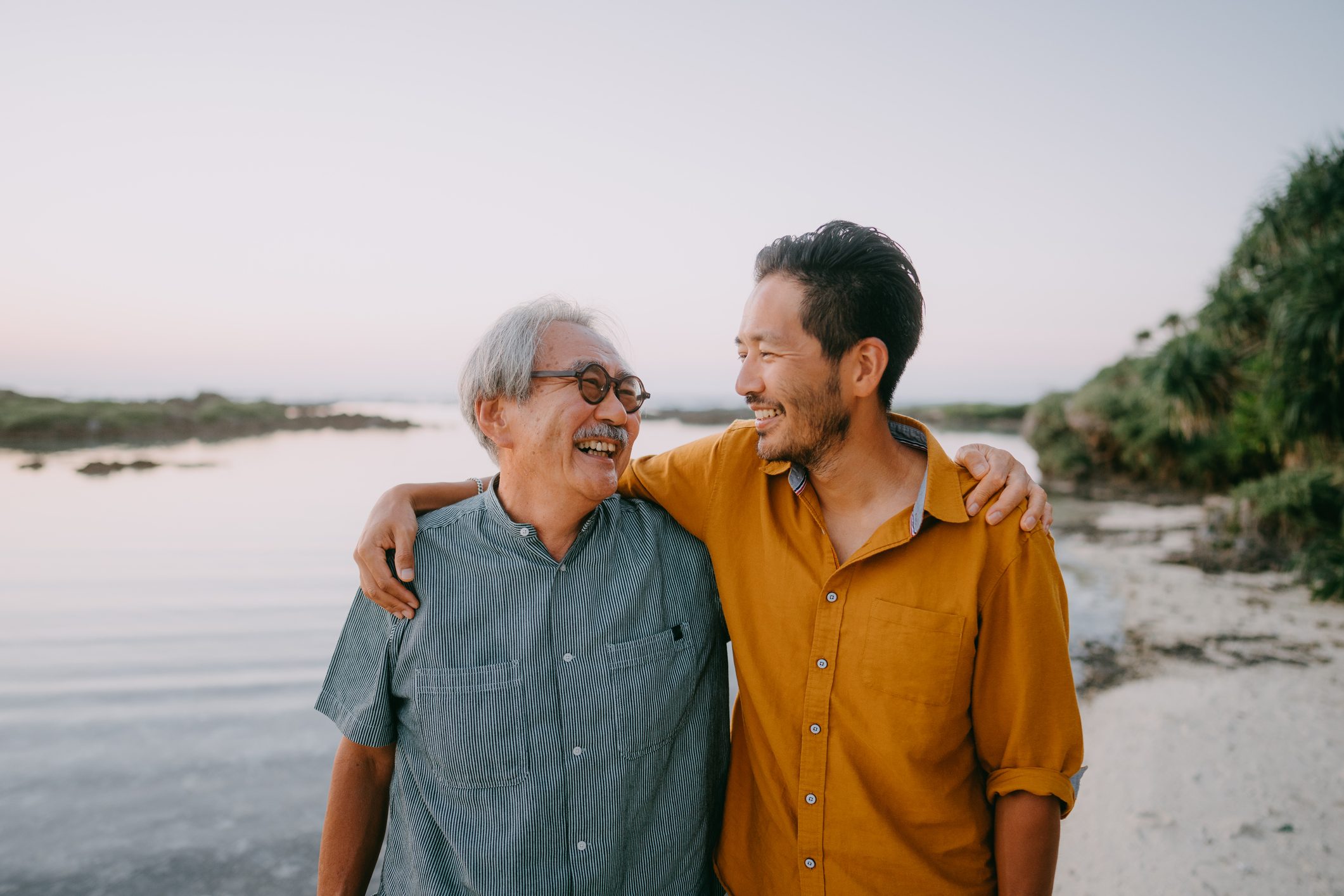 Senior father and adult son having a good time on beach at sunset