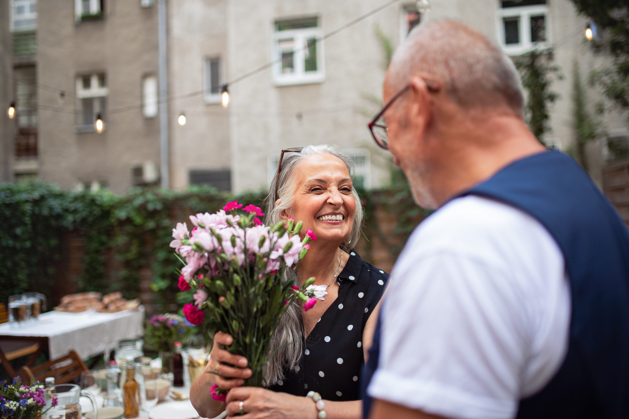 Happy senior woman getting bouquet from her husband outdoors in garden.