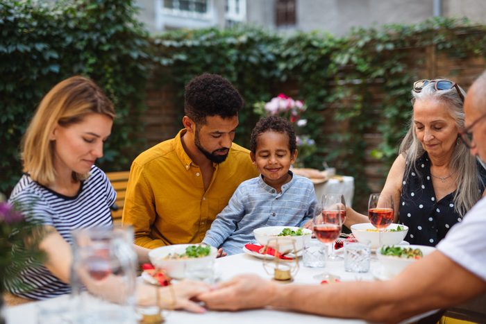 Portrait of multiracial three generations family praying together when dining outdoors in front or back yard.