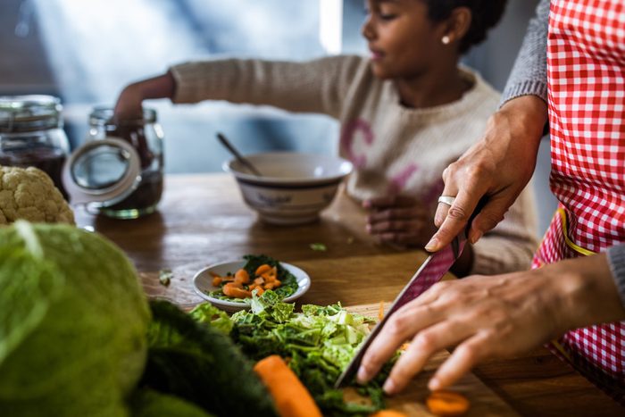 Close up of unrecognizable woman cutting fresh salad while preparing food with her daughter in the kitchen.