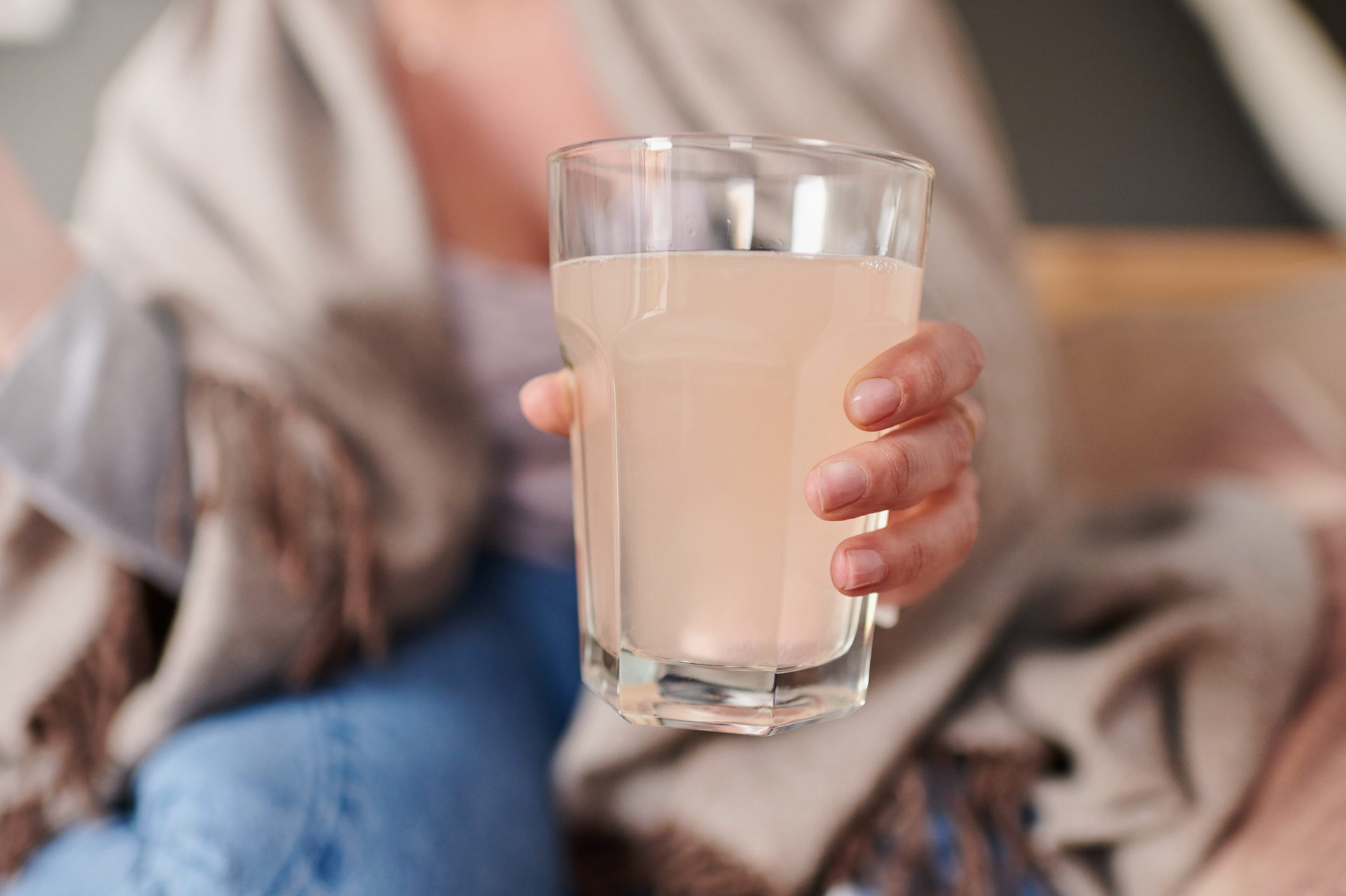 Cropped shot of a woman holding up a drink while sitting at home