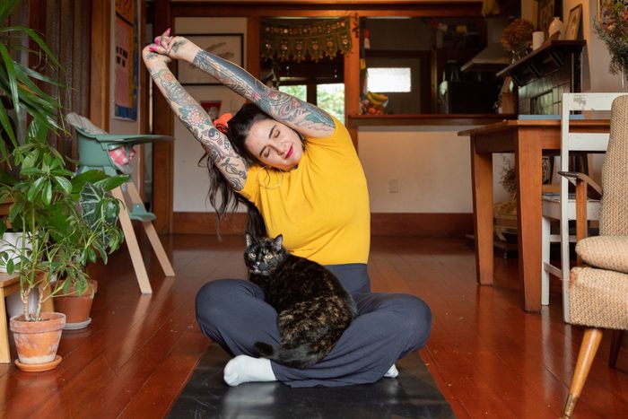 Tattooed woman stretching at home with cat in lap
