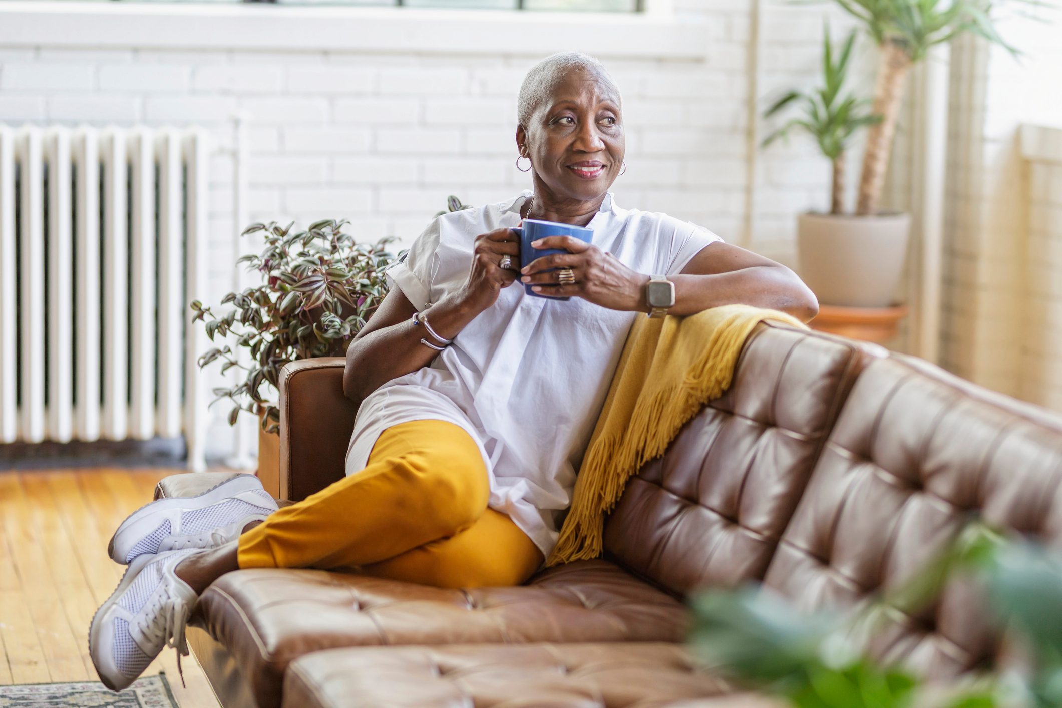 Beautiful senior woman smiling while sitting on sofa and drinking tea at home