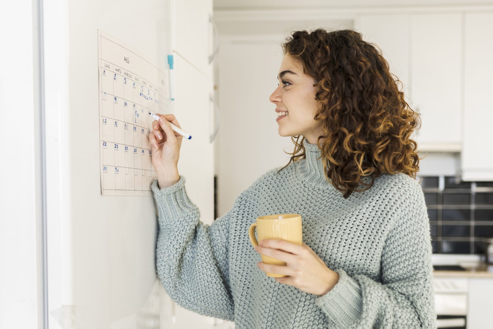 woman looking at calendar in the kitchen, holding a mug