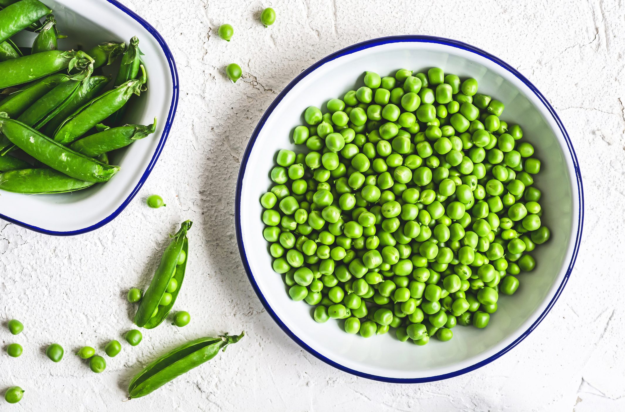 Green peas in a bowl with a bowl of pea shells to the side