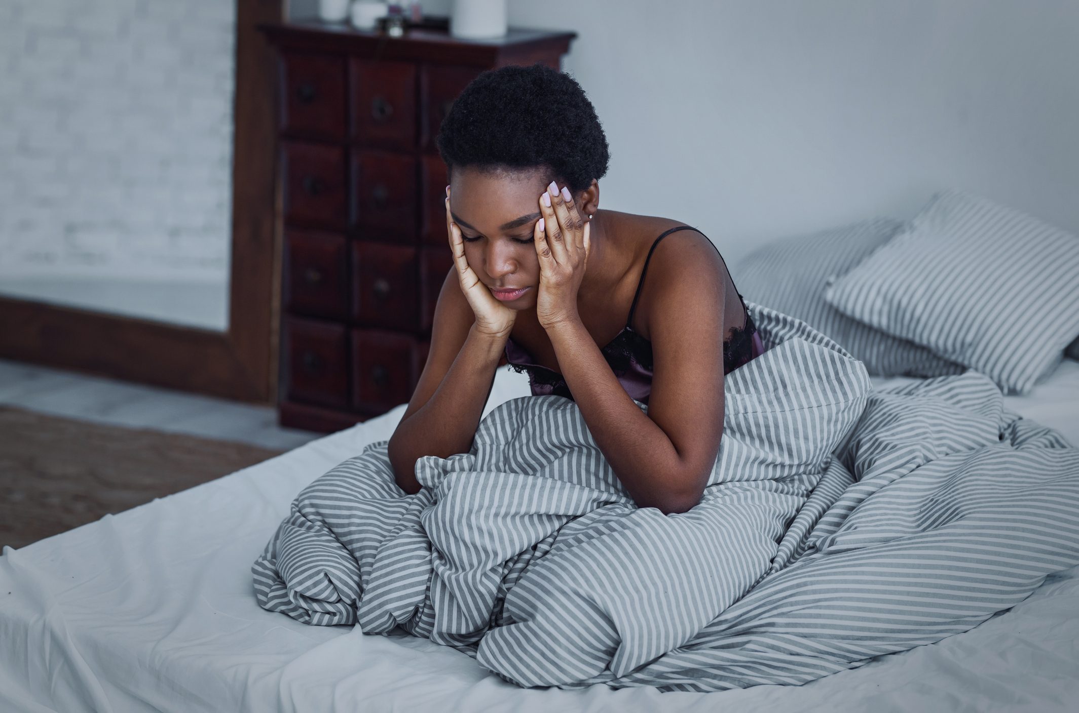 Girl woke up at night, sitting on bed and holding her hands to head