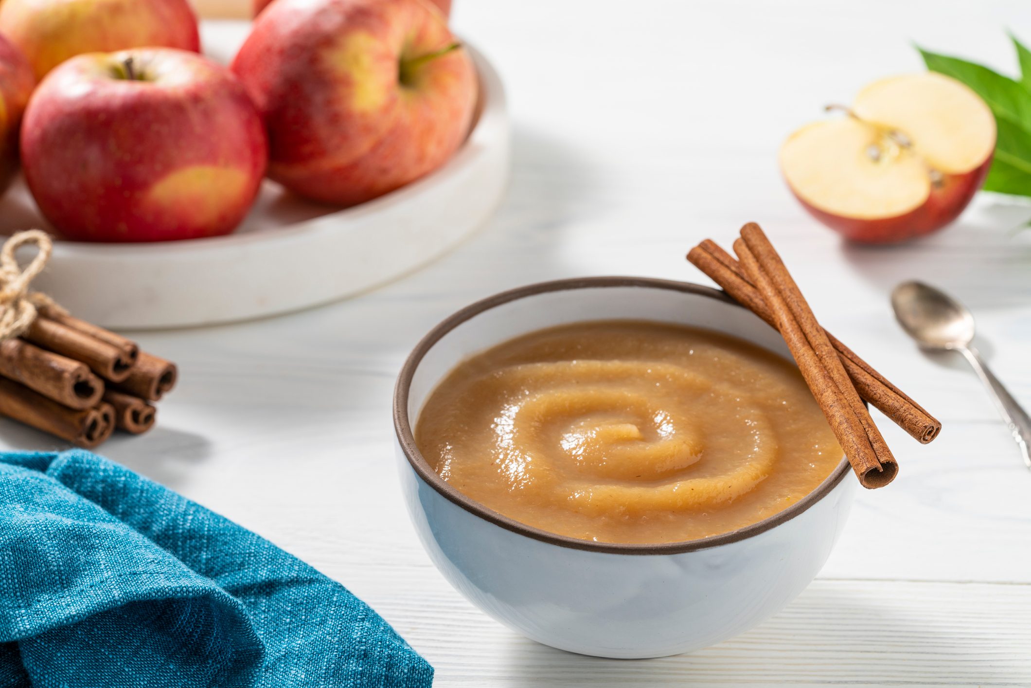 Apple sauce or apple pureed compote homemade with raw red apples on white wooden background