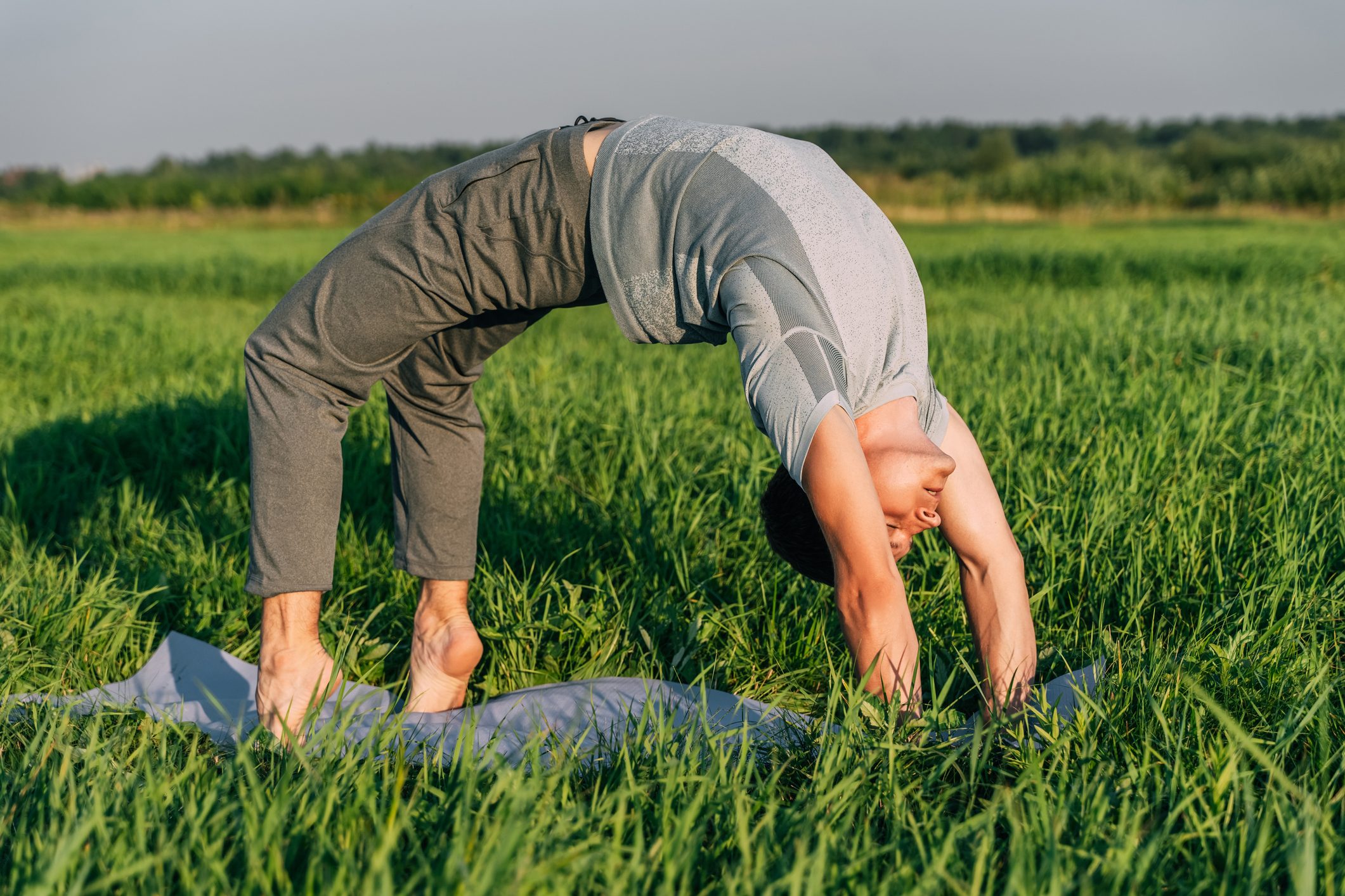 Young man doing yoga in the field at sunset. Summer day, wellness concept.