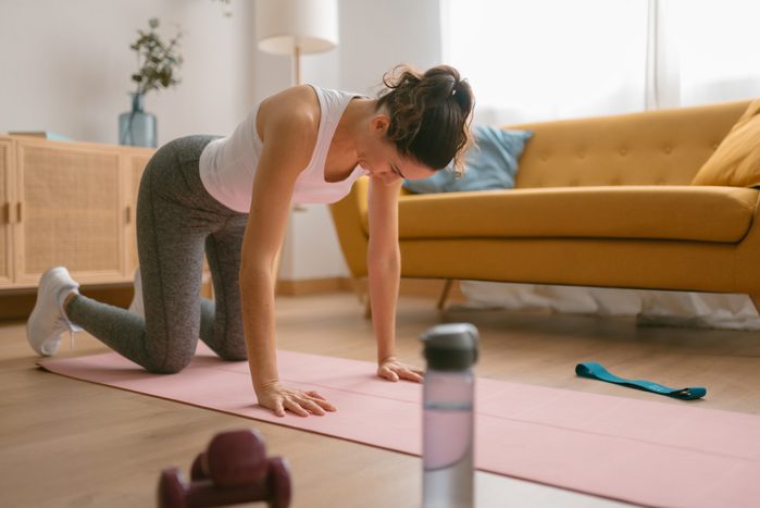 Young woman stretching at home after weight training.