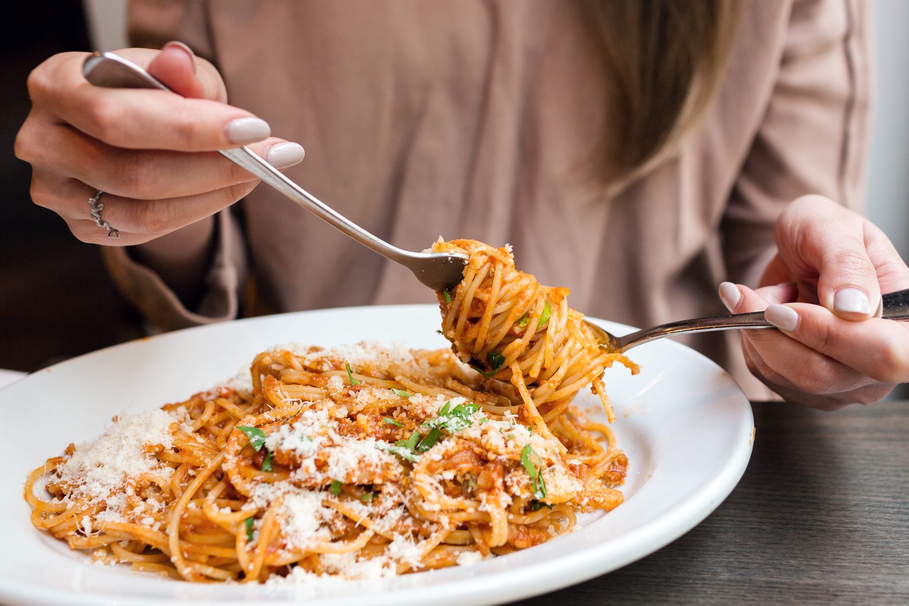 girl eats Italian pasta with tomato, meat. Close-up spaghetti Bolognese wind it around a fork with a spoon. Parmesan cheese