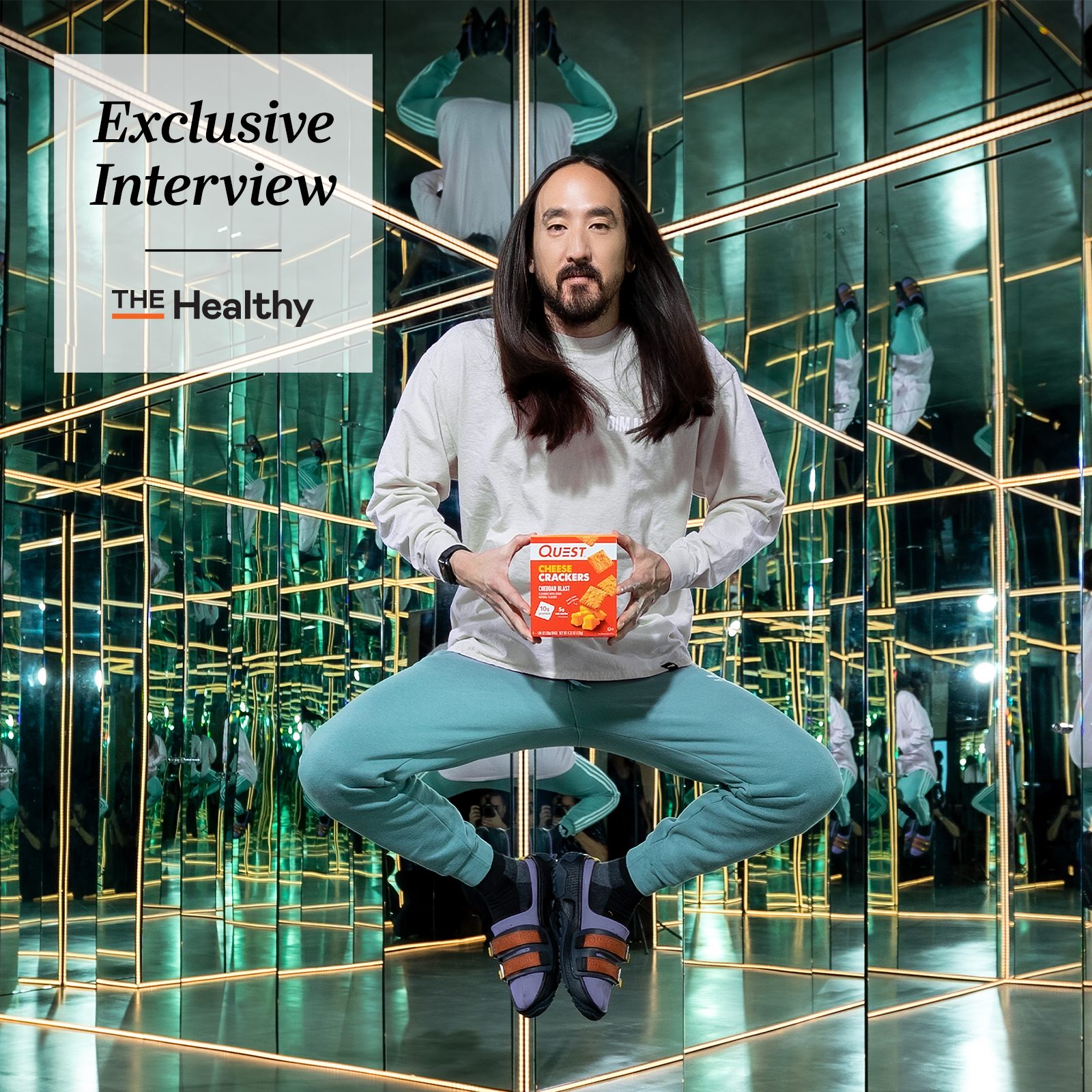 Steve Aoki floating holding a box of quest crackers with the healthy exclusive interview template