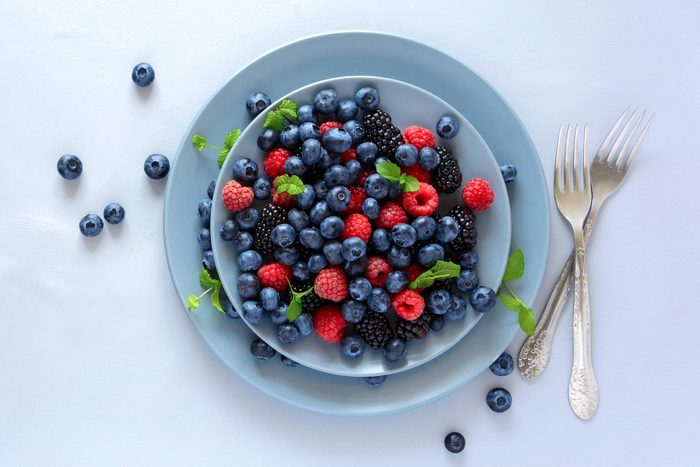 Fruit salad with blackberry, blueberry, raspberry and mint leaves on wooden gray background. Flat lay. Top view