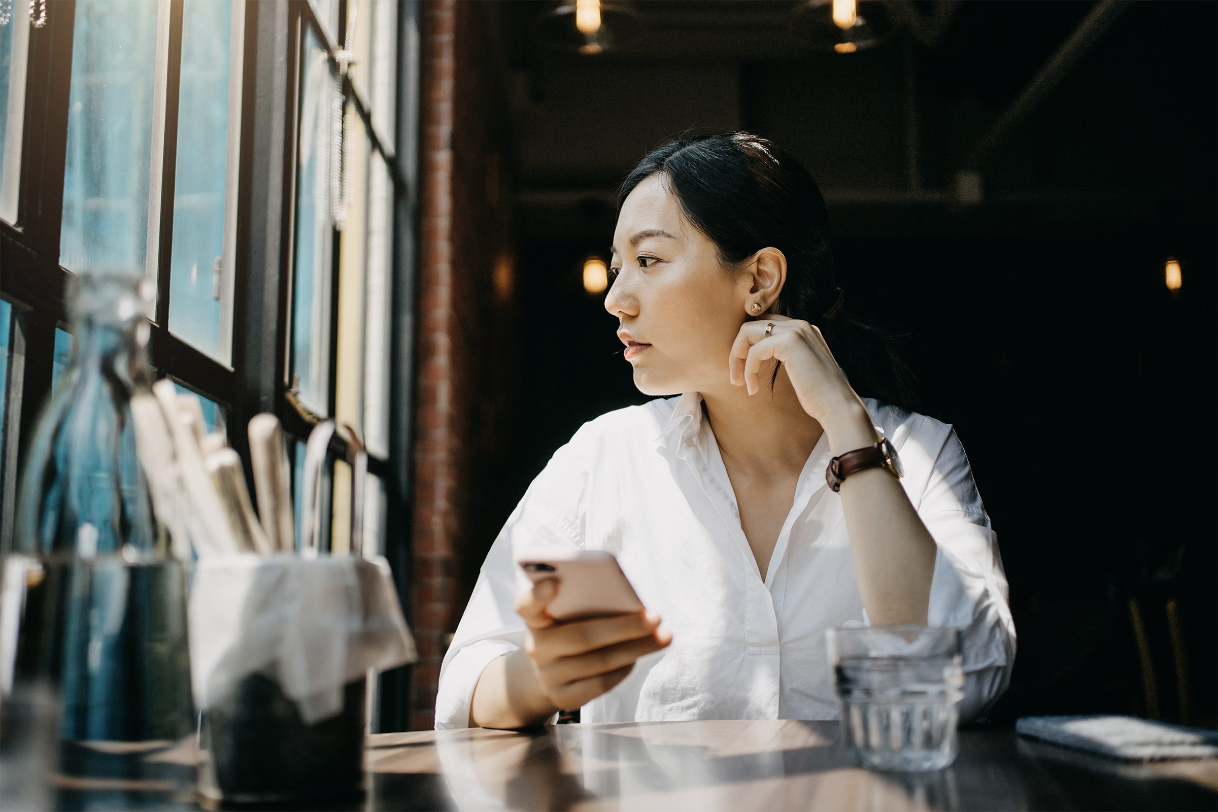 Young woman in a cafe looking out the window with phone in hand