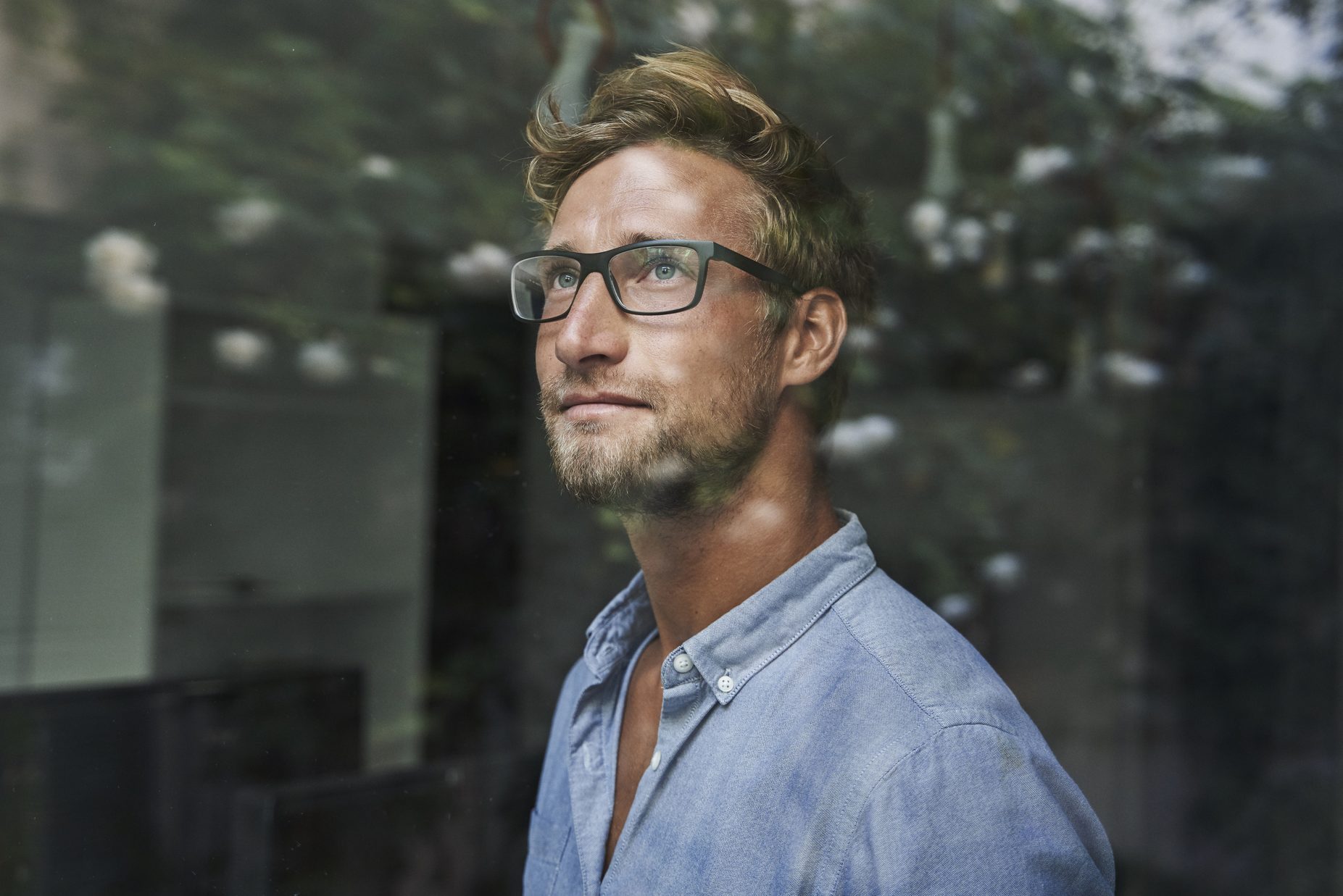 Casual young businessman behind windowpane in office