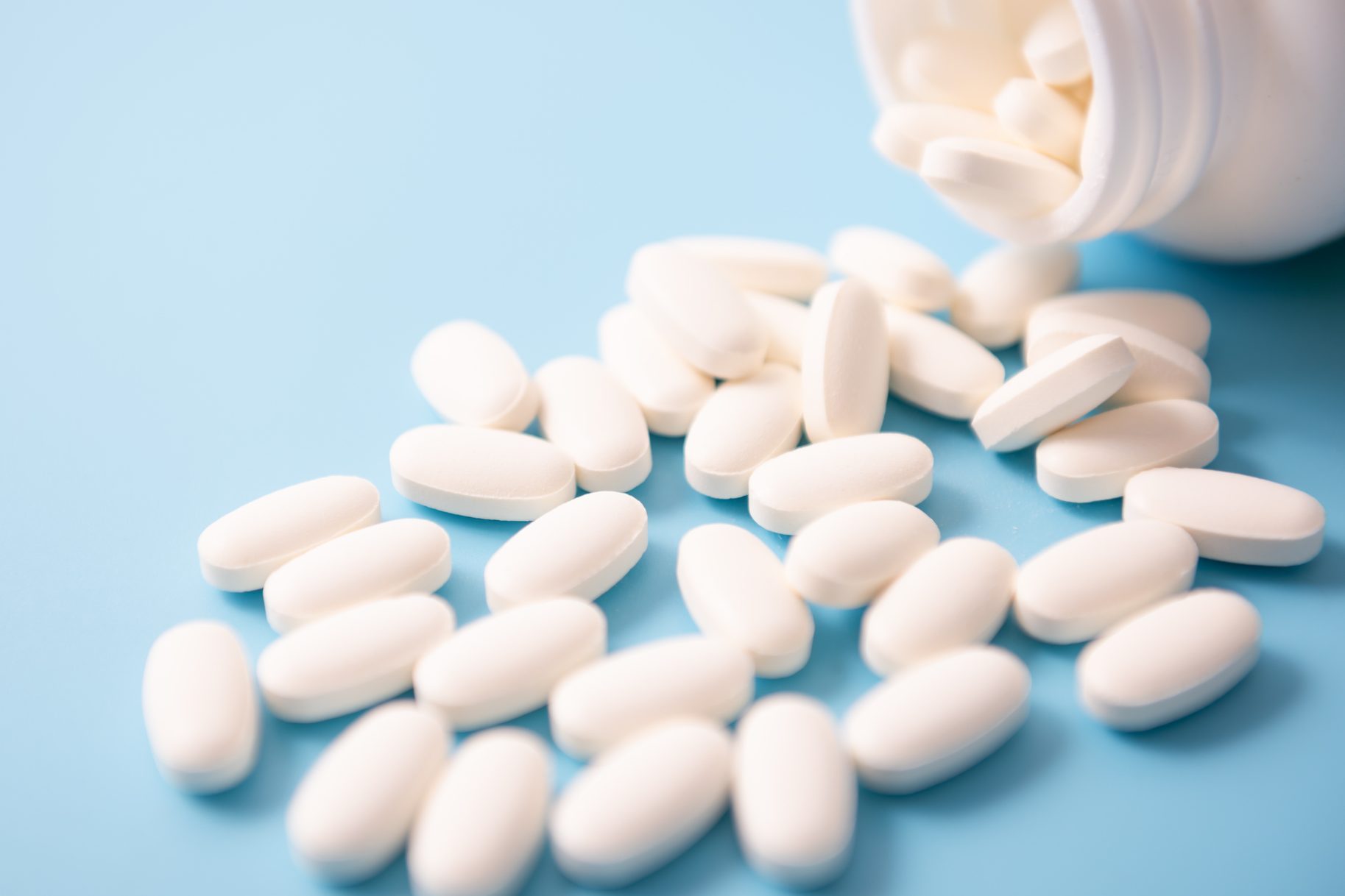 Calcium Pills Pouring Out Of Bottle On Blue Background