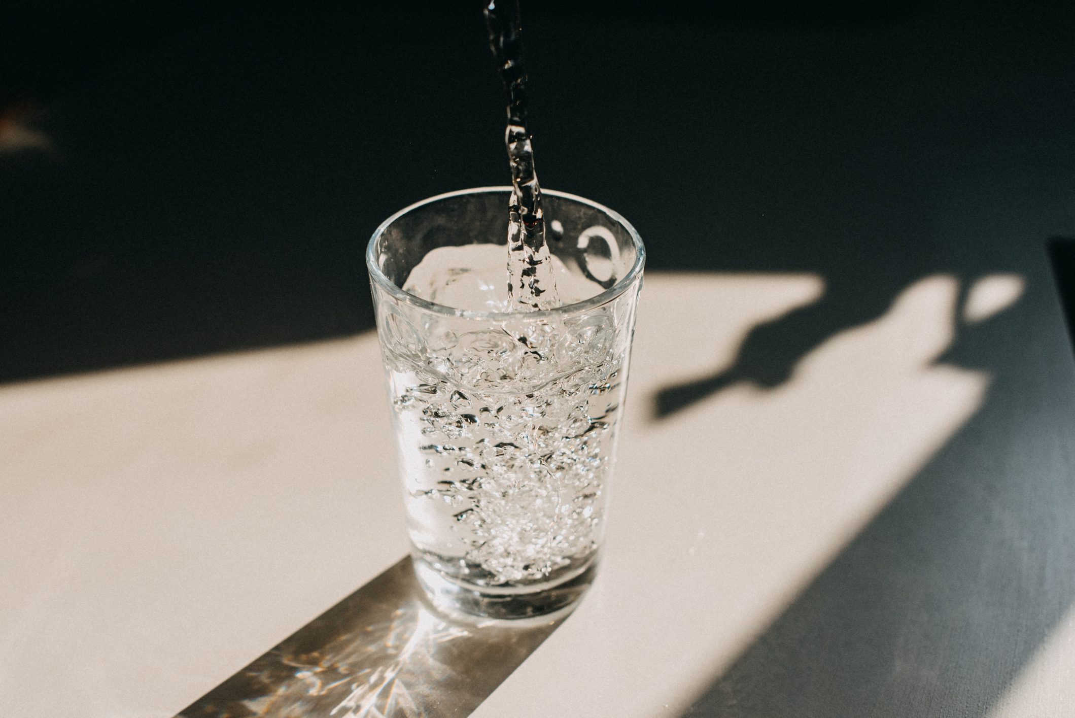 Water being poured in a glass of water that cast a beautiful shadow on a white kitchen countertop