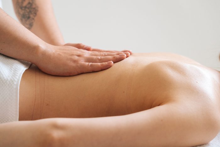 Side of male masseur massaging small of back of young woman lying on massage table at spa salon.