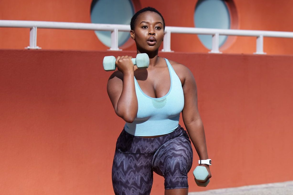 Shot of a young woman on a gym mat using dummbells against an urban background