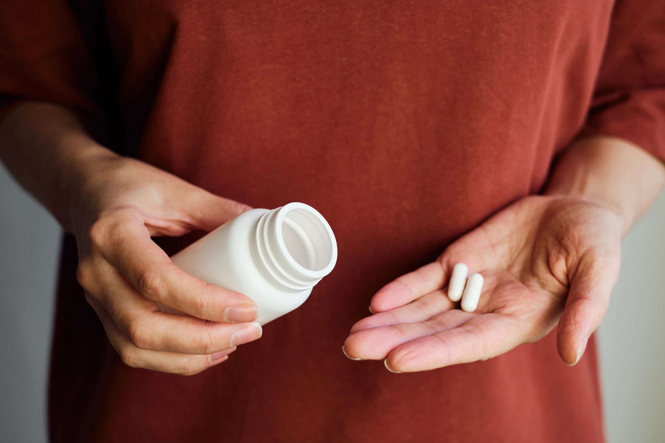 A woman pours pills or vitamins from a jar onto her hand. Taking vitamins or medications. The concept of health care, medicine, pharmacies, disease prevention. A jar with pills or vitamins in the hand