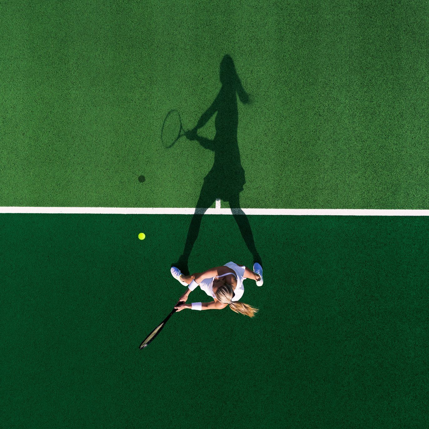 Drone shot above a female tennis player and her shadow, England, United Kingdom