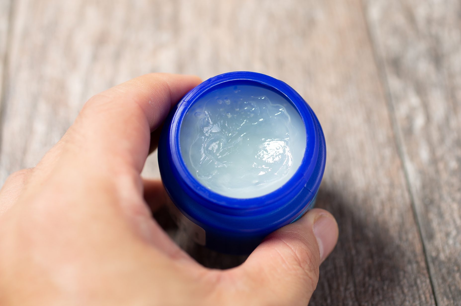 A view of a hand holding a container of topical cough suppressant ointment.