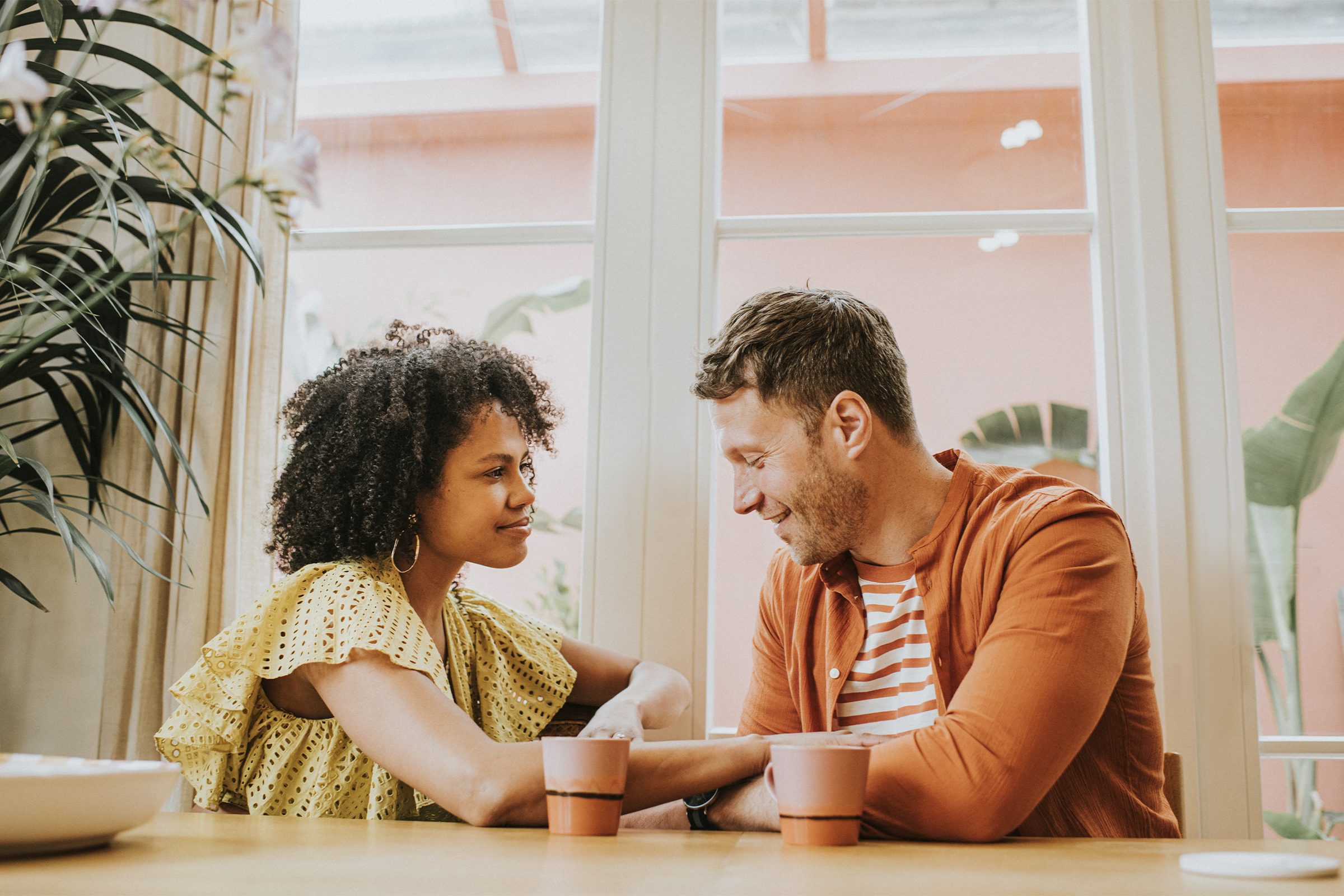 A young couple sitting at a dining table sipping hot drinks and talking