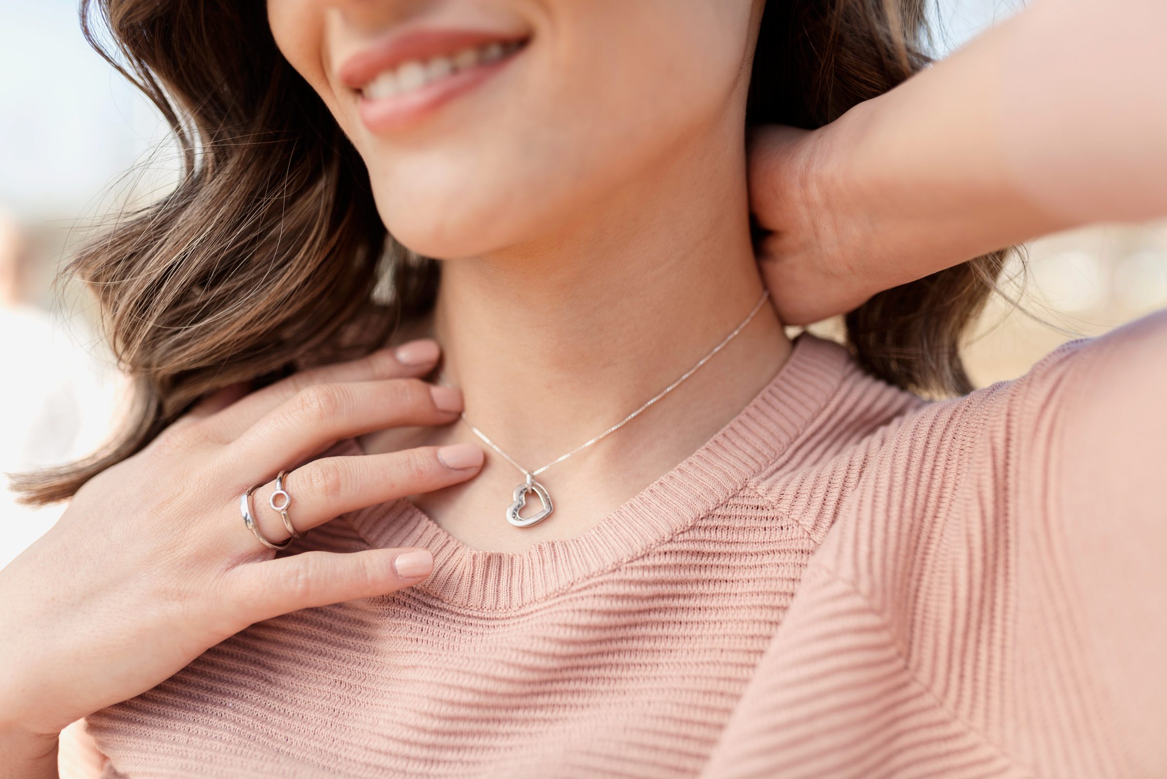 Close-up shot of a happy, beautiful woman putting on the silver necklace